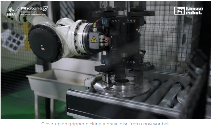 Close-up on gripper picking a brake disc from conveyor belt